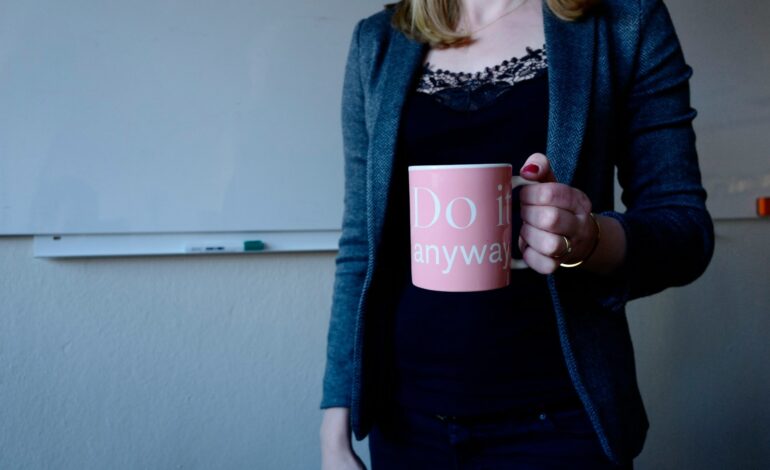 A confident woman holding a coffee cup with the motivational phrase 'Do it Anyway,' symbolizing empowerment and determination in female leadership.